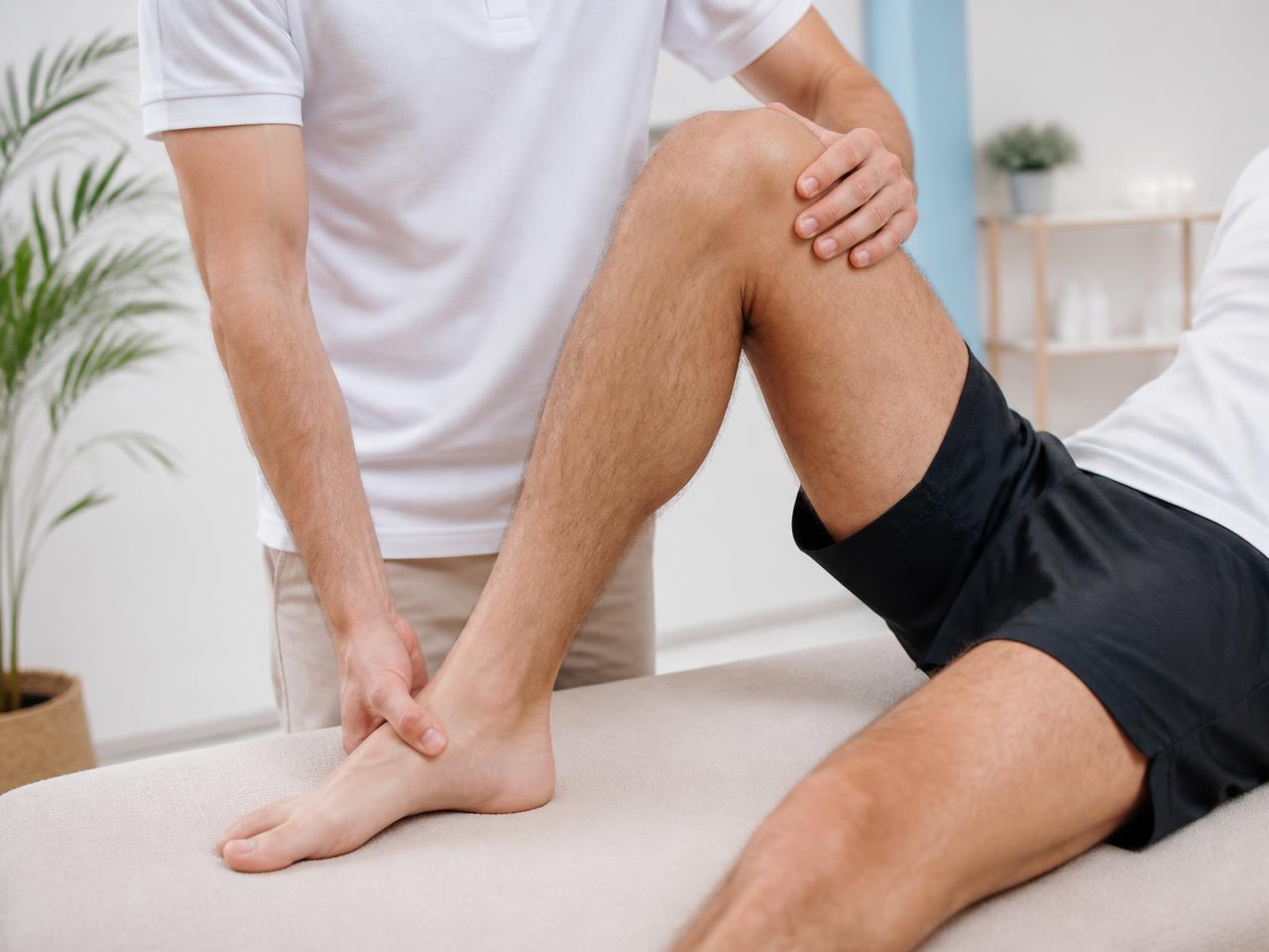 Fisioterapeuta asistiendo la movilidad controlada de rodilla y tobillo de una persona deportista